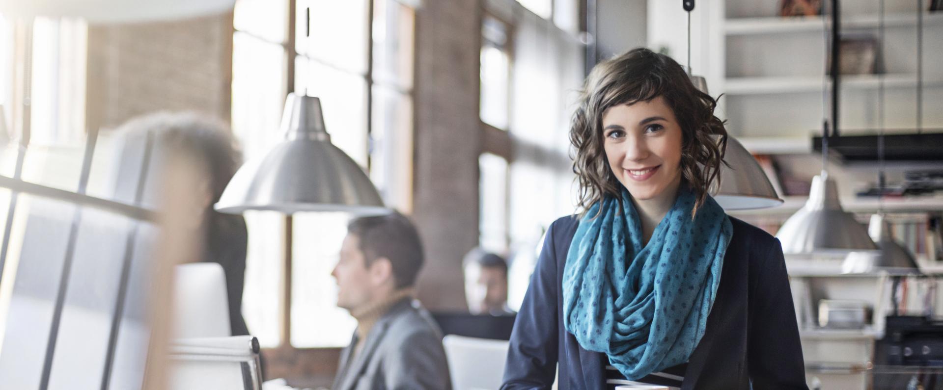 woman holding a cup of coffee standing in front of a desk