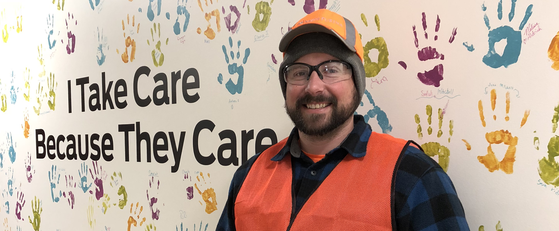 Man standing in front of wall of handprints which reads 'I Take Care Because They Care'