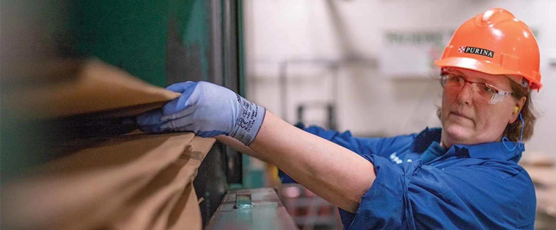 Woman working in factory with hard hat, safety glasses, and gloves