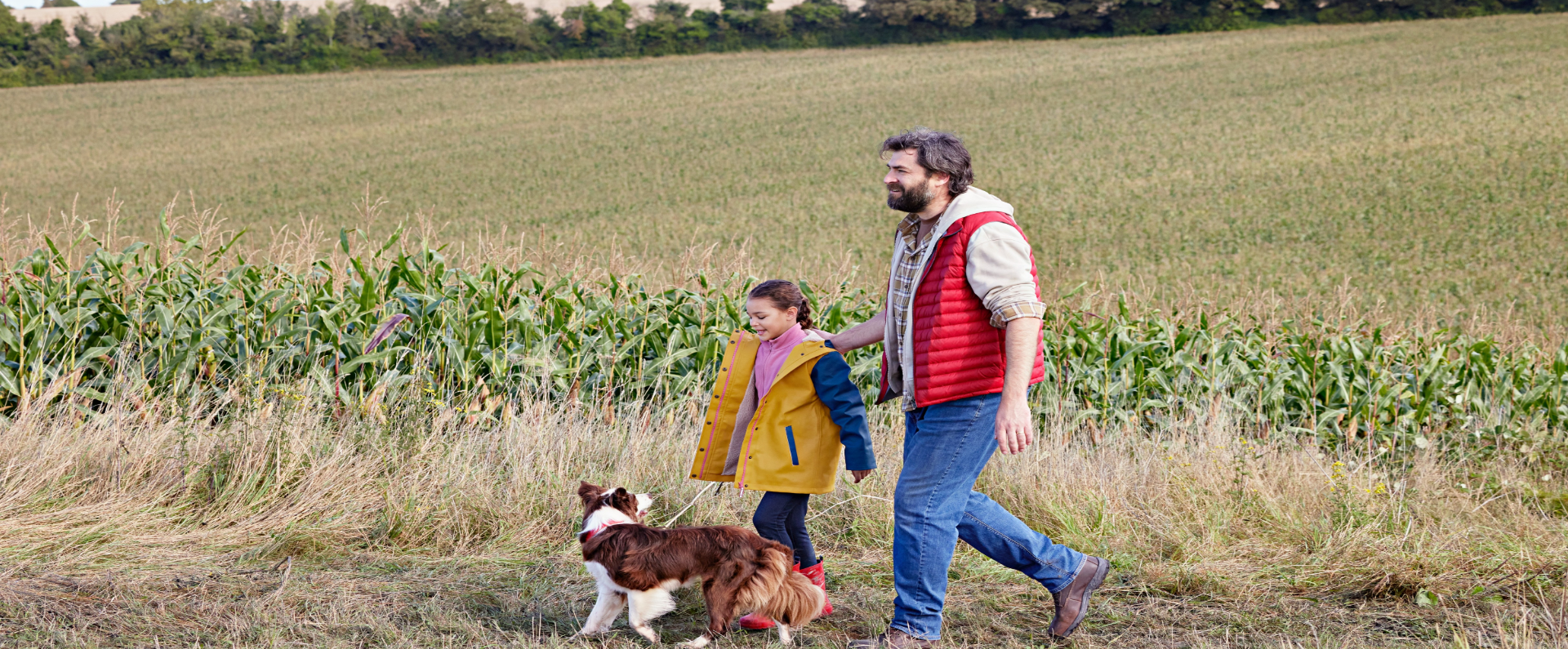 Father and daughter walking in field with dog